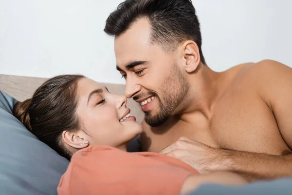 Sin camisa musculoso hombre sonriendo cerca sexy novia en cama en casa - foto de stock