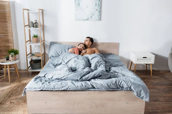 Young woman sleeping near shirtless man under grey blanket in modern bedroom — Stock Photo