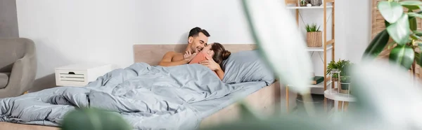 Homem alegre abraçando namorada na cama em primeiro plano borrado, banner — Fotografia de Stock