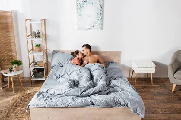 Mujer joven abrazando hombre musculoso sin camisa en amplio dormitorio moderno - foto de stock