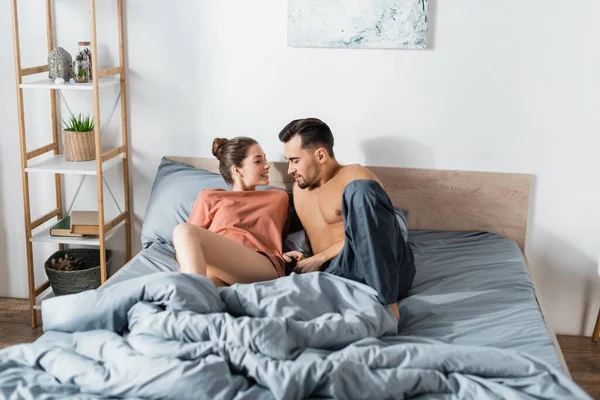 Lächelnde Frau im T-Shirt im Gespräch mit sexy Freund zu Hause im Bett — Stockfoto