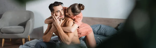Mulher apaixonada abraçando o homem sem camisa deitado na cama em primeiro plano borrado, banner — Fotografia de Stock