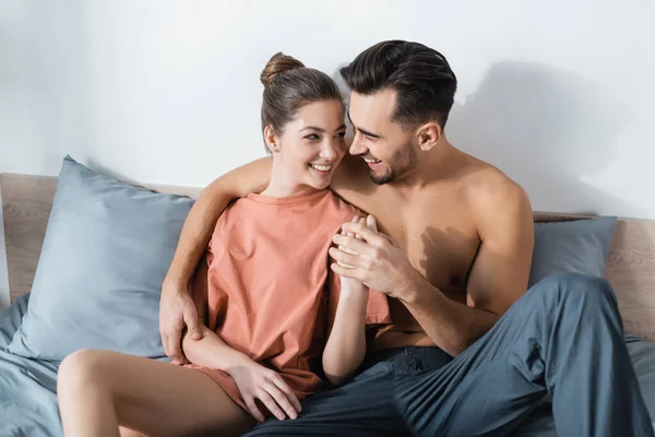 Glückliches junges Paar Händchen haltend und einander auf dem Bett anschauend — Stockfoto