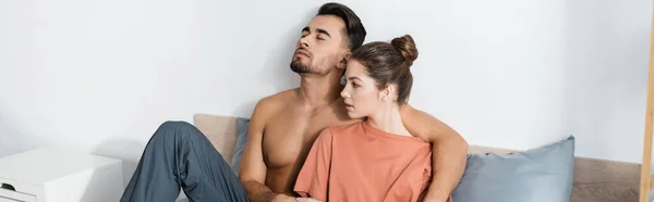 Hemdloser Mann mit geschlossenen Augen umarmt Freundin im T-Shirt auf dem Bett zu Hause, Banner — Stockfoto