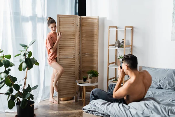 Homme torse nu musclé avec caméra vintage prenant des photos de petite amie sexy posant près diviseur de chambre — Photo de stock