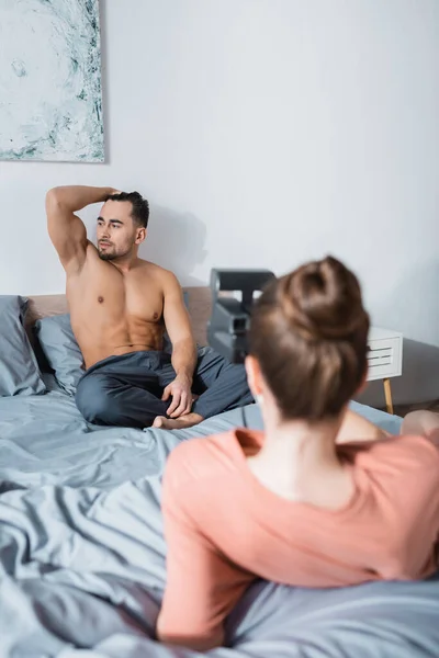 Sexy sin camisa hombre posando en la cama cerca borrosa novia con vintage cámara - foto de stock