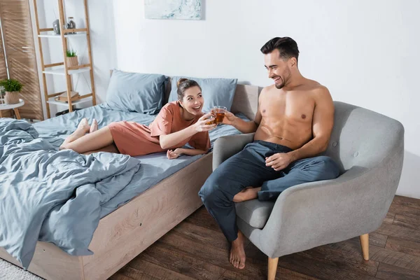 Joyeux jeune couple griller avec des tasses à thé dans la chambre à coucher à la maison — Photo de stock