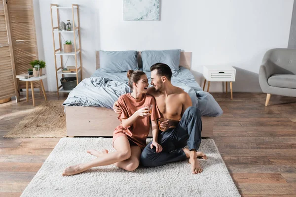 Fröhliches Paar mit Teetassen, die auf dem Boden im Schlafzimmer sitzen und einander anlächeln — Stockfoto
