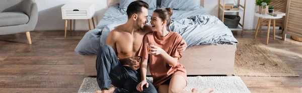 Coppia sorridente guardarsi mentre si siede sul pavimento in camera da letto con tazze da tè, banner — Foto stock