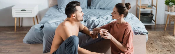 Jeune couple sexy tenant des tasses à thé et se regardant tout en parlant dans la chambre à coucher, bannière — Photo de stock