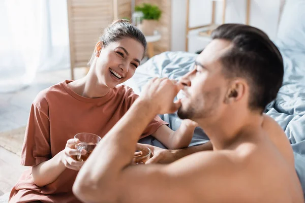 Young and joyful woman with cup of tea looking at boyfriend on blurred foreground — Stock Photo