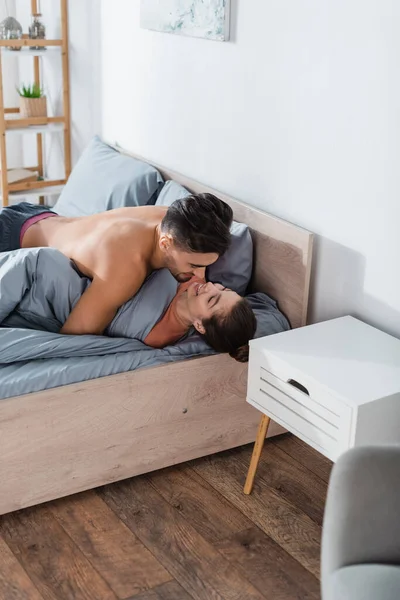 Shirtless man hugging smiling girlfriend lying under grey blanket — Stock Photo