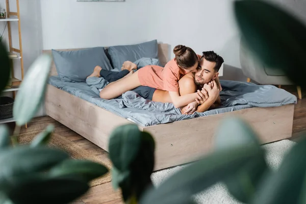 Сексуальна жінка приймає без сорочки хлопець лежить на ліжку на розмитому передньому плані — стокове фото