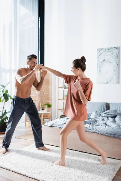 Full length of cheerful couple fighting while having fun in bedroom — Stock Photo