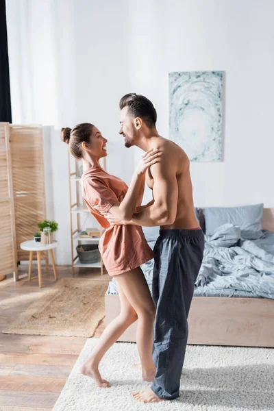 Vista laterale di felice giovane coppia sorridente e ballare in camera da letto — Foto stock