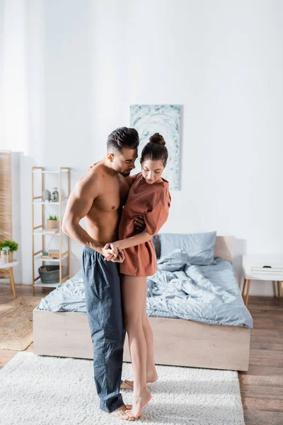 Young man in pajama pants teaching girlfriend in t-shirt to dance in bedroom — Stock Photo