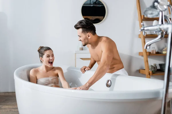 Excited woman with open mouth taking bath near shirtless boyfriend — Stock Photo