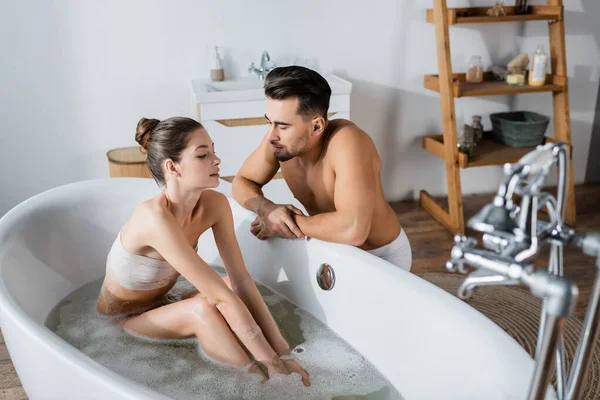 Сексуальная молодая женщина принимает ванну рядом с парнем без рубашки с мускулистым туловищем — стоковое фото