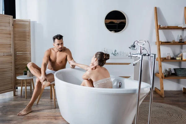 Sexy hombre en calzoncillos cogido de la mano con joven novia relajarse en la bañera - foto de stock