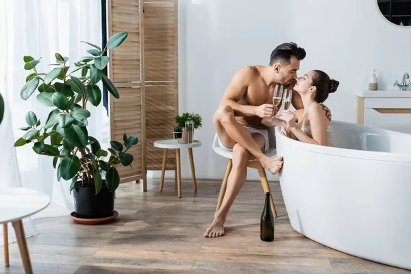 Sexy hombre en calzoncillos y mujer en bañera besos y tintineo copas de champán - foto de stock