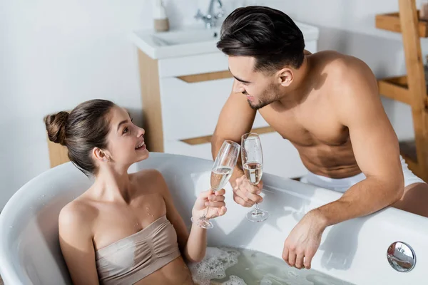 Gioiosa donna in vasca da bagno clinking bicchieri di champagne con sexy fidanzato muscolare — Foto stock