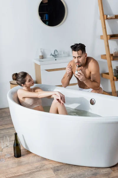 Shirtless muscular man lighting cigarette near sexy girlfriend relaxing in bathtub — Stock Photo