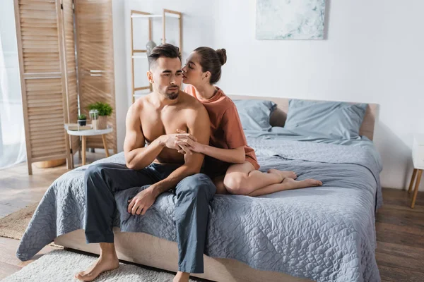 Jovem mulher sexy de mãos dadas com homem sem camisa e beijando-o no quarto — Fotografia de Stock