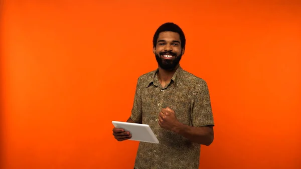 Positive african american young man with beard holding digital tablet on orange background — Stock Photo