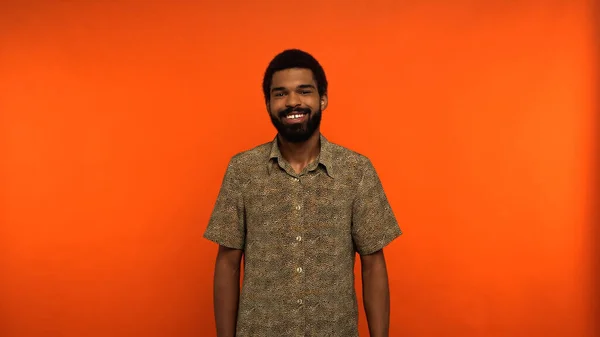 Homme afro-américain joyeux avec barbe debout en chemise sur fond orange — Photo de stock