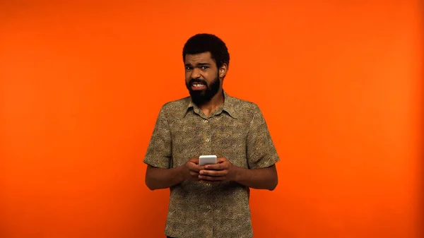 Desagradado afro-americano homem mensagens smartphone no fundo laranja — Fotografia de Stock