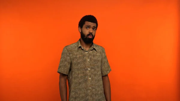 Surprised african american man with beard looking at camera while standing on orange background — Stock Photo