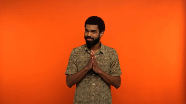 Sly african american man with beard looking at camera while gesturing on orange background — Stock Photo