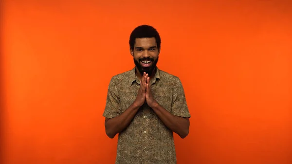Sly african american man with beard looking at camera while smiling on orange background — Stock Photo