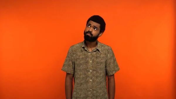 Pensive african american man with beard looking away while standing on orange background — Stock Photo