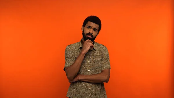 Thoughtful african american man in shirt looking away while standing on orange background — Stock Photo