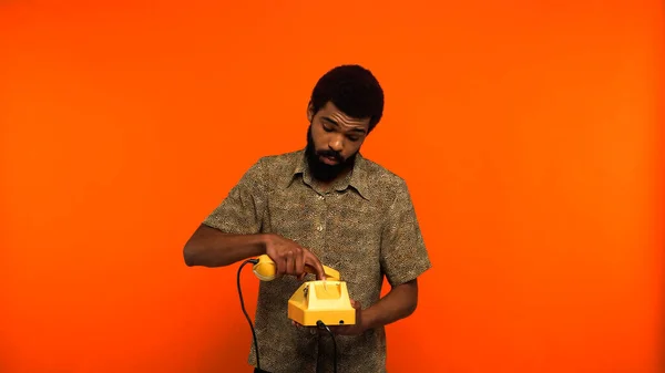 Young african american man with beard using yellow retro telephone on orange background — Stock Photo