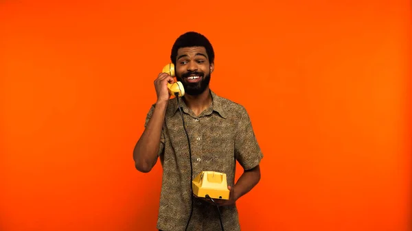 Gioioso afro americano uomo avendo chiamata su retro telefono su sfondo arancione — Foto stock