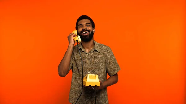 Joyeux homme afro-américain avec barbe parlant sur un téléphone vintage sur fond orange — Photo de stock