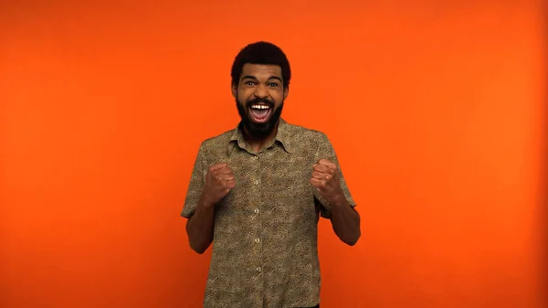 Aufgeregter afrikanisch-amerikanischer junger Mann mit Bart jubelt auf orangefarbenem Hintergrund — Stockfoto