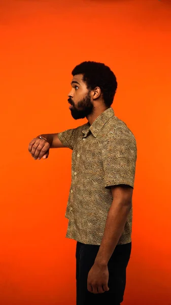 Vista verticale del giovane americano africano sorpreso con orologio da polso che distoglie lo sguardo sull'arancione — Foto stock