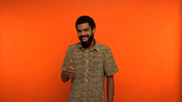 Jeune homme afro-américain étonné avec la barbe montrant pouce vers le haut sur fond orange — Photo de stock