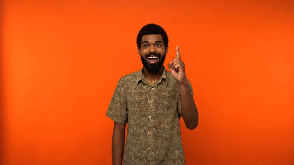 Glücklich afrikanisch-amerikanischer junger Mann zeigt Ideenschild auf orangefarbenem Hintergrund — Stockfoto