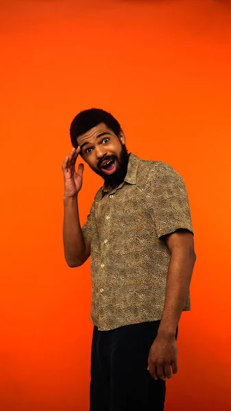 Vertical view of surprised african american man with beard and opened mouth on orange — Stock Photo