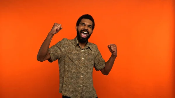 Aufgeregter afrikanisch-amerikanischer Mann mit Bart zeigt Jubelgeste auf orangefarbenem Hintergrund — Stockfoto