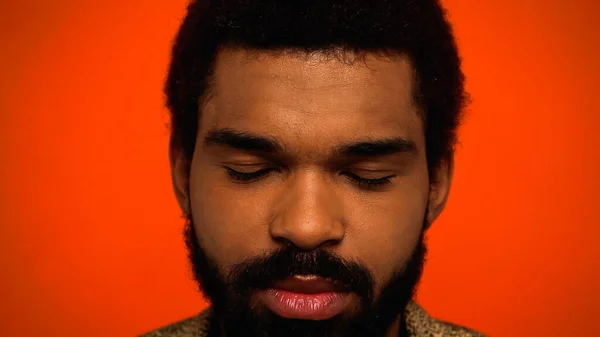 Close up de jovem e barbudo homem americano africano com olhos fechados meditando isolado em laranja — Fotografia de Stock