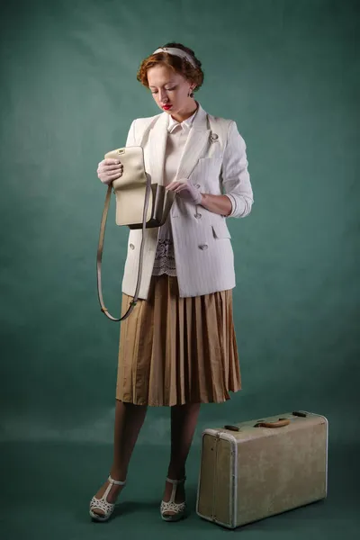 一个穿着复古风格的年轻女人 脚上有一只手提箱 正在检查她钱包里的东西 工作室肖像 免版税图库照片