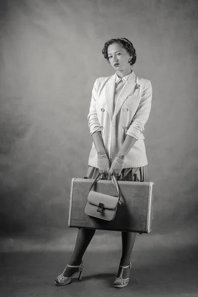年轻的女人穿着复古风格的衣服 手里拿着一个手提箱和一个手提包 黑白照片演播室 — 图库照片