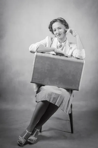 年轻的女人穿着复古风格的衣服 坐在椅子上 膝盖上抱着一个手提箱 黑白照片演播室 图库照片
