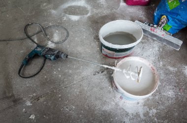Construction equipment. A spatula, a bucket of solution and an electric drill with a mixing attachment. The picture was taken in Russia, in an industrial building