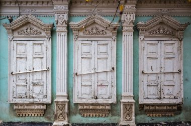 Dekor ve sıva oyulmuş eski bir evin kapalı panjurlu üç penceresi, ön cephenin bir parçası. Rusya, Orenburg şehri